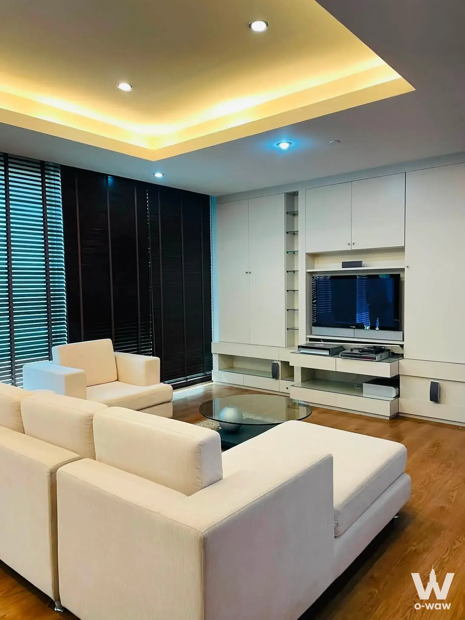 Spacious living room in 3-bed Ascott Sathorn Bangkok condo with wood floors, white sofa, and built-in entertainment unit