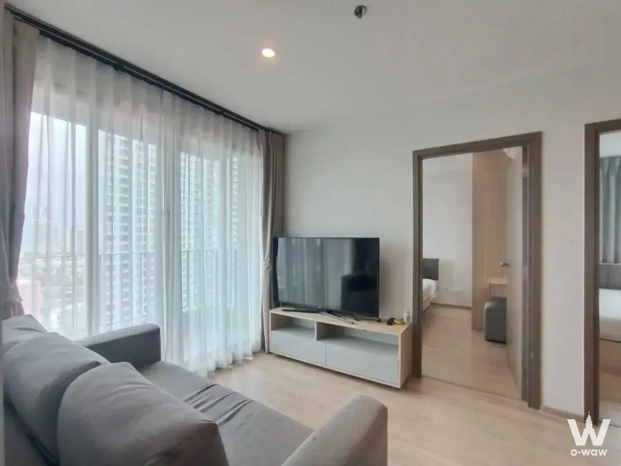 Ideo O2 2-bed condo living room with grey sofa, TV, and city skyline view