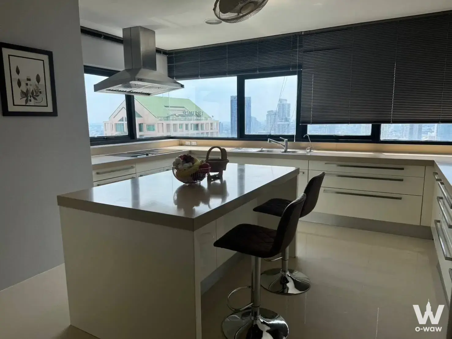 Modern condo kitchen with glossy white cabinets, breakfast island, and city skyline views in Sathorn Gardens 4-bed for sale