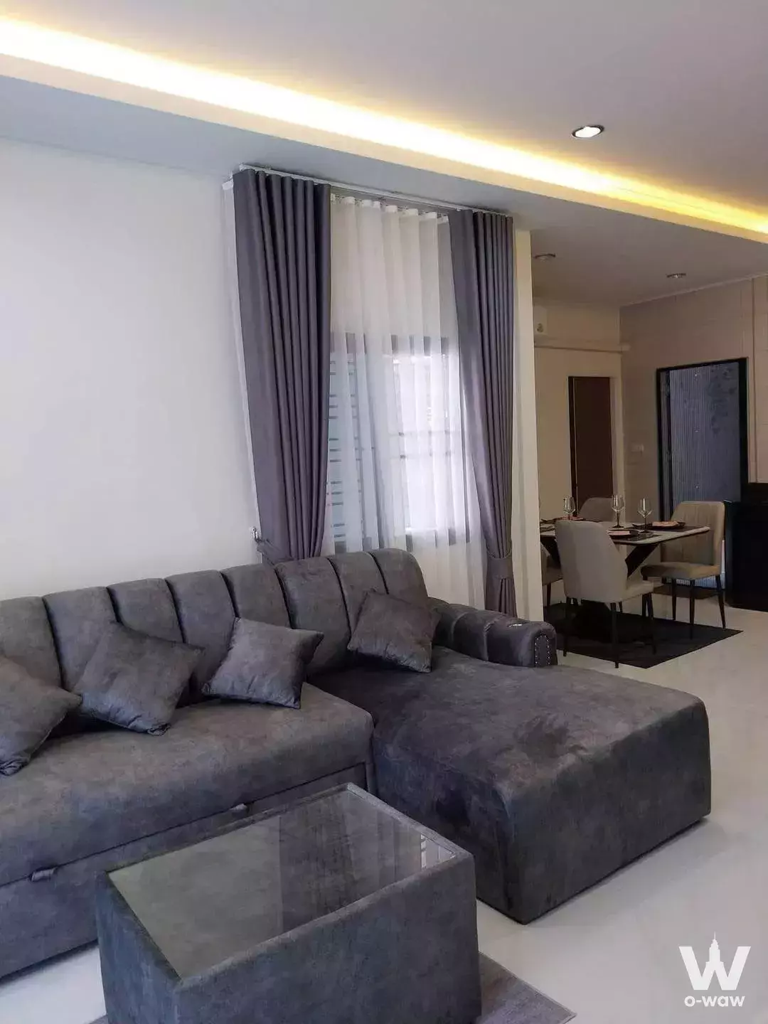 Modern open-plan living and dining area with grey sectional sofa and floor-to-ceiling windows in 2-bed condo for rent Siam