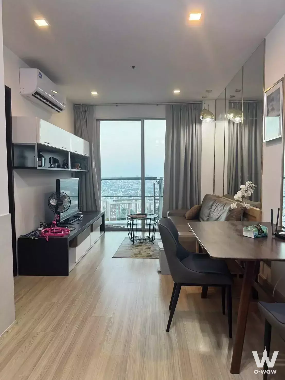 Modern 1-bed condo living room in Sky Walk Residences with grey sofa, city view balcony, and mirrored dining wall