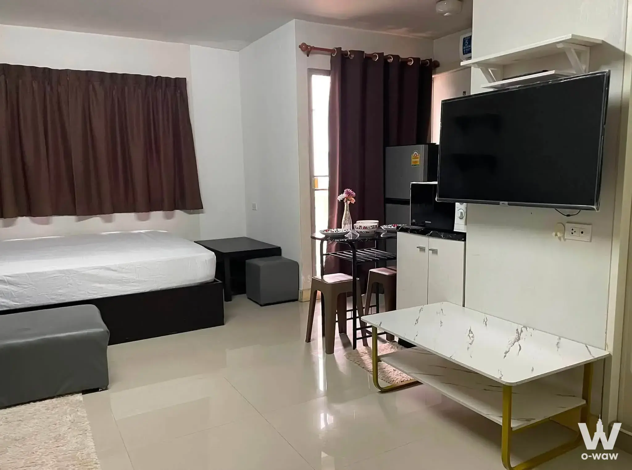 Queen bed and compact kitchenette in a furnished 1-bed condo for sale at Lumpini Condo Town Bodindecha-Ramkhamhaeng