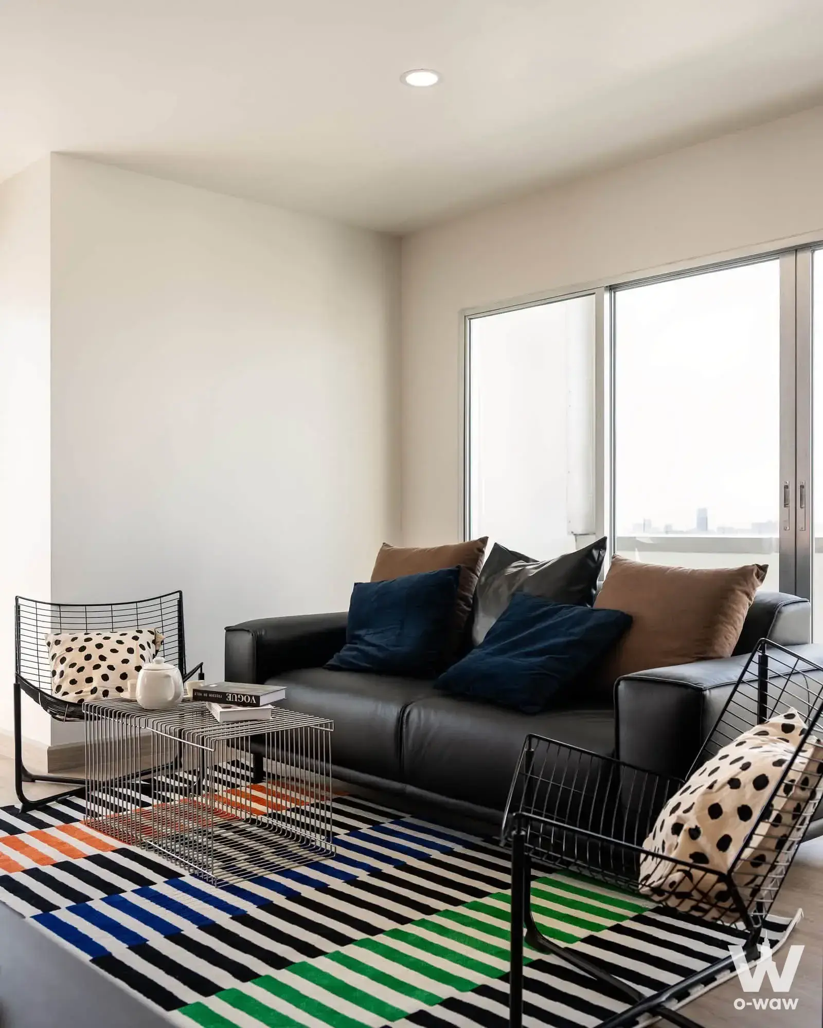The Sarin Place 2-bed condo living room features a black leather sofa, bold striped rug and city skyline view