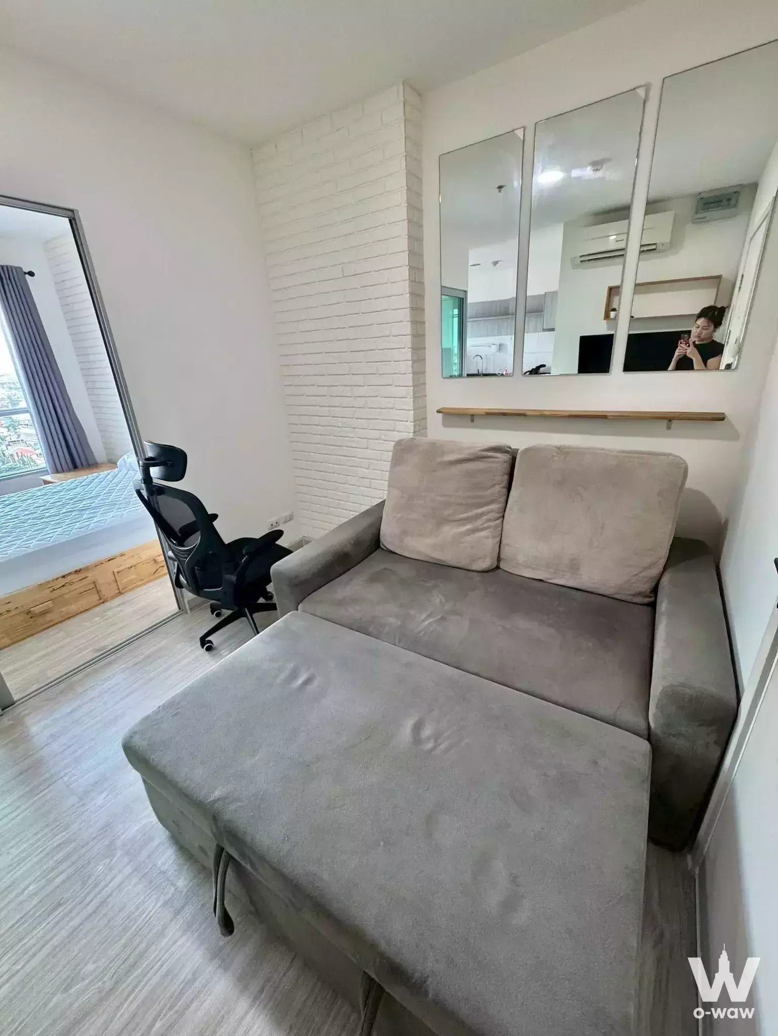 1-bed condo for rent in Aspire Ngamwongwan featuring grey sectional sofa and faux brick accent wall