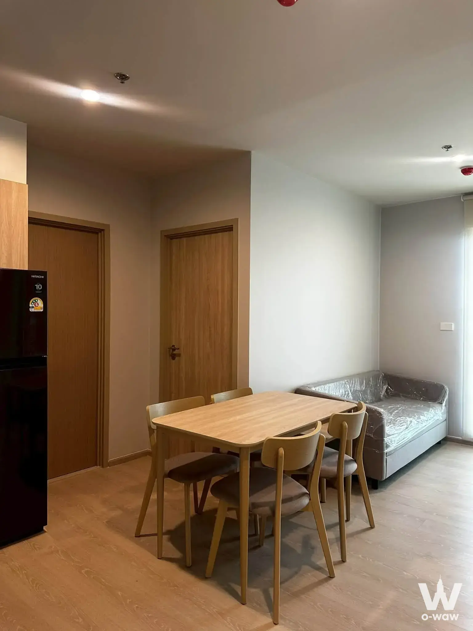 Open-plan living area in Nue Mega Plus Bangna featuring a dining set and grey sofa on light oak flooring