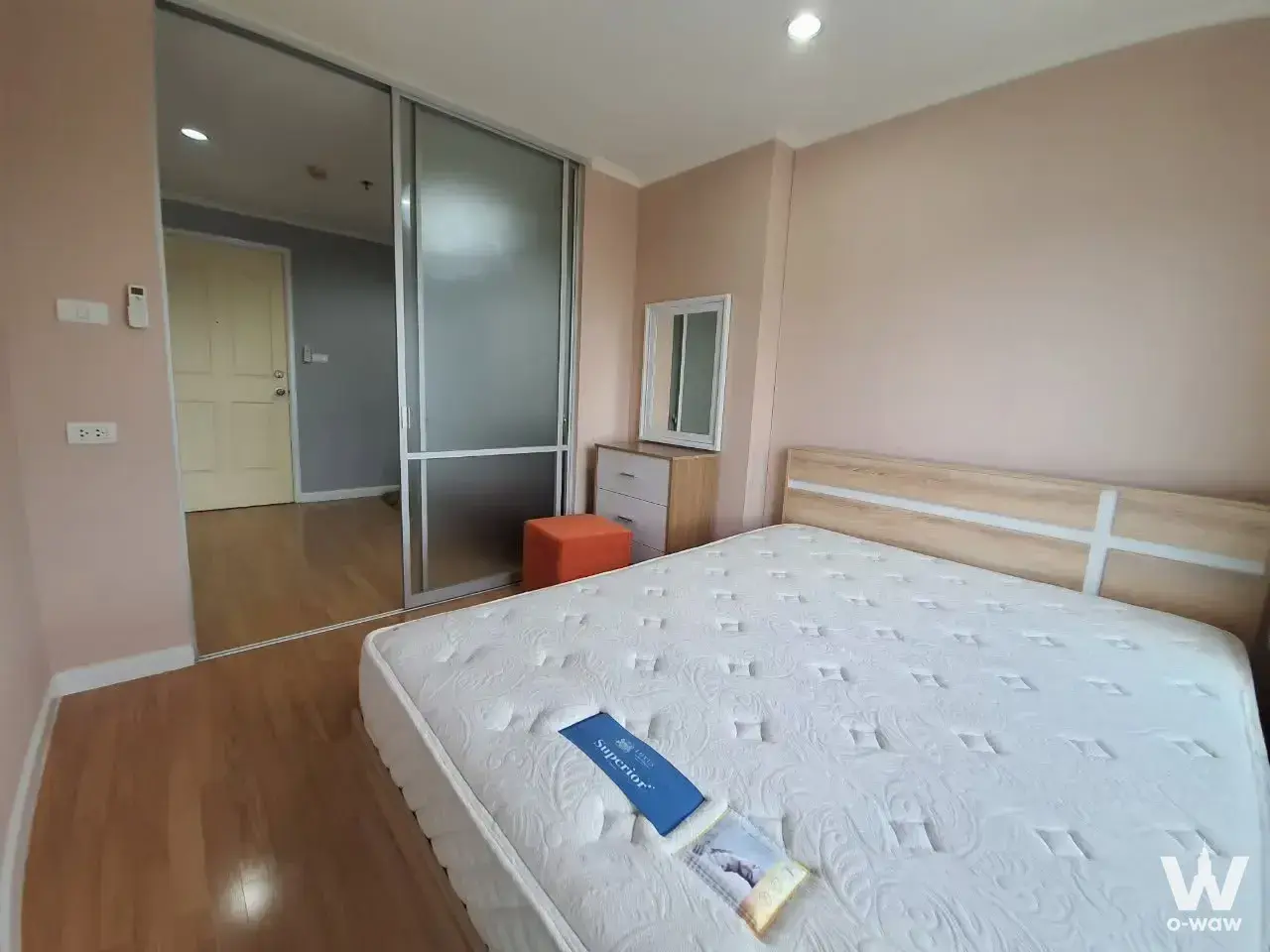 Unfurnished bedroom in Lumpini Ville Bangkhae condo with pink walls, mirrored wardrobe, and oak headboard