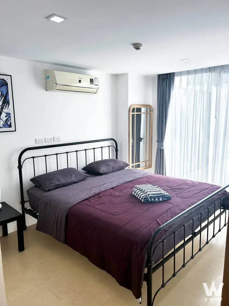 Aurora Pratumnak 2-bed condo bedroom has black metal double bed, purple-grey bedding, sheer curtains and floor mirror