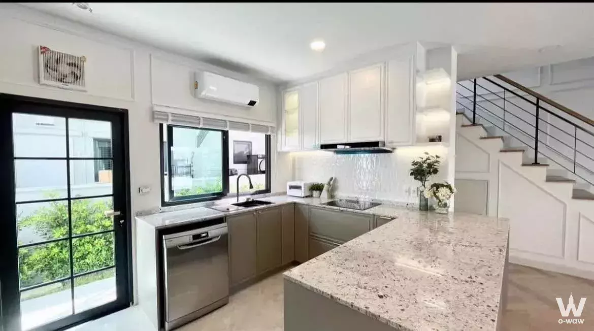 Modern L-shaped kitchen with grey cabinets, granite island, and glass door to patio in 4-bed house for rent in Centro Bangna