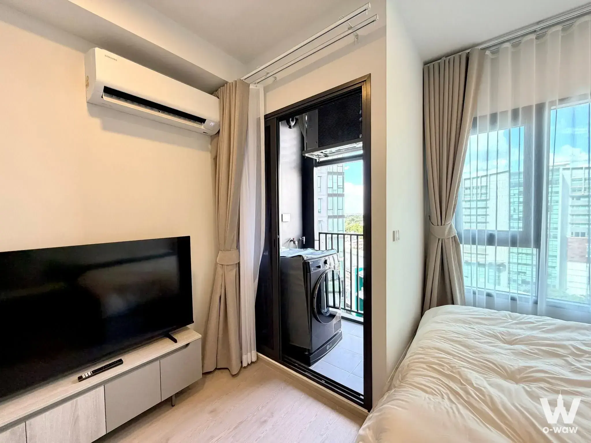 Bright 1-bed condo bedroom in COBE Kaset-Sripatum with city views, TV console, and balcony laundry area