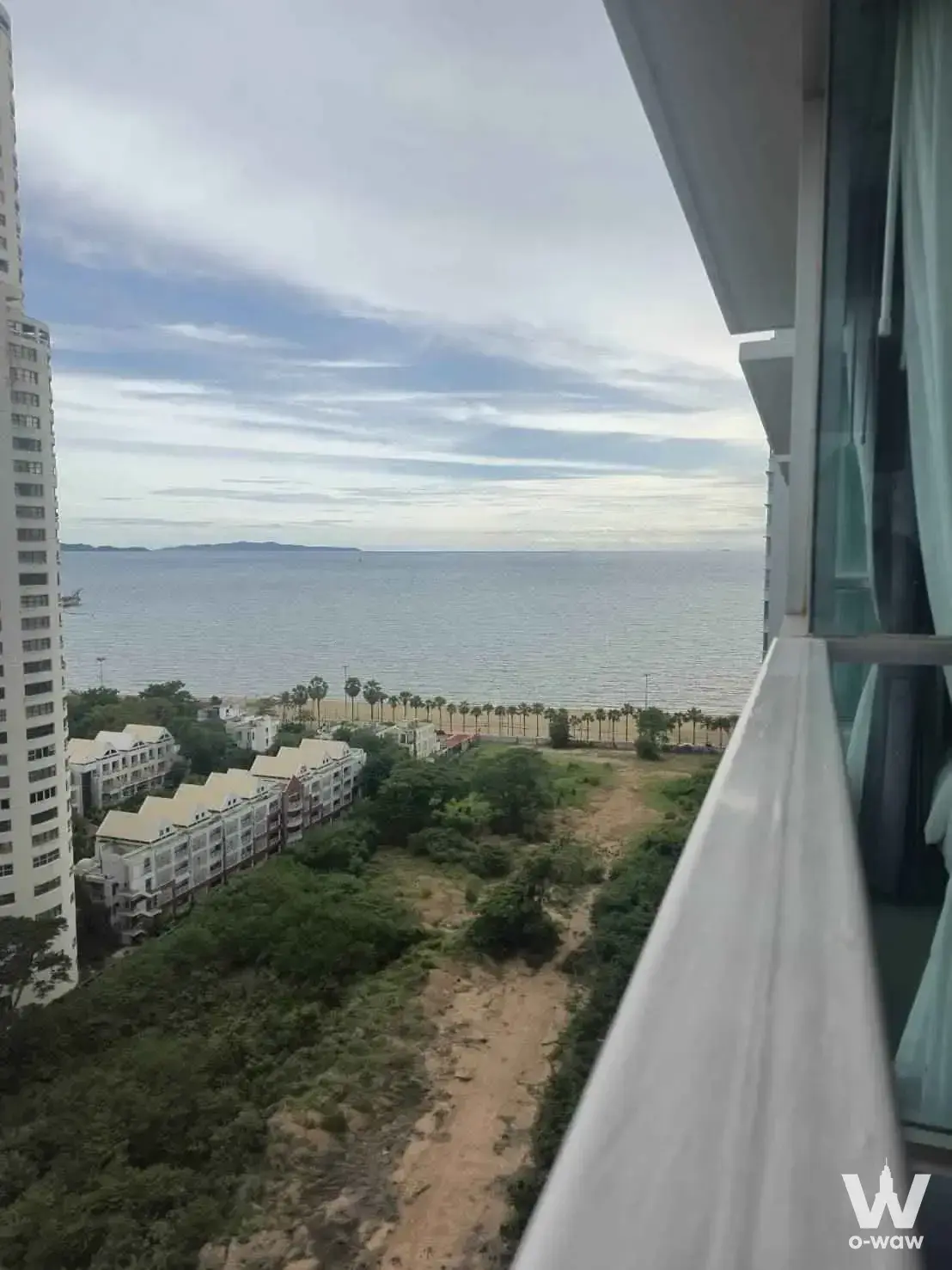 High-floor balcony with glass doors overlooking sea, beach, and palm trees at Lumpini Park Beach Jomtien A 1-bed condo