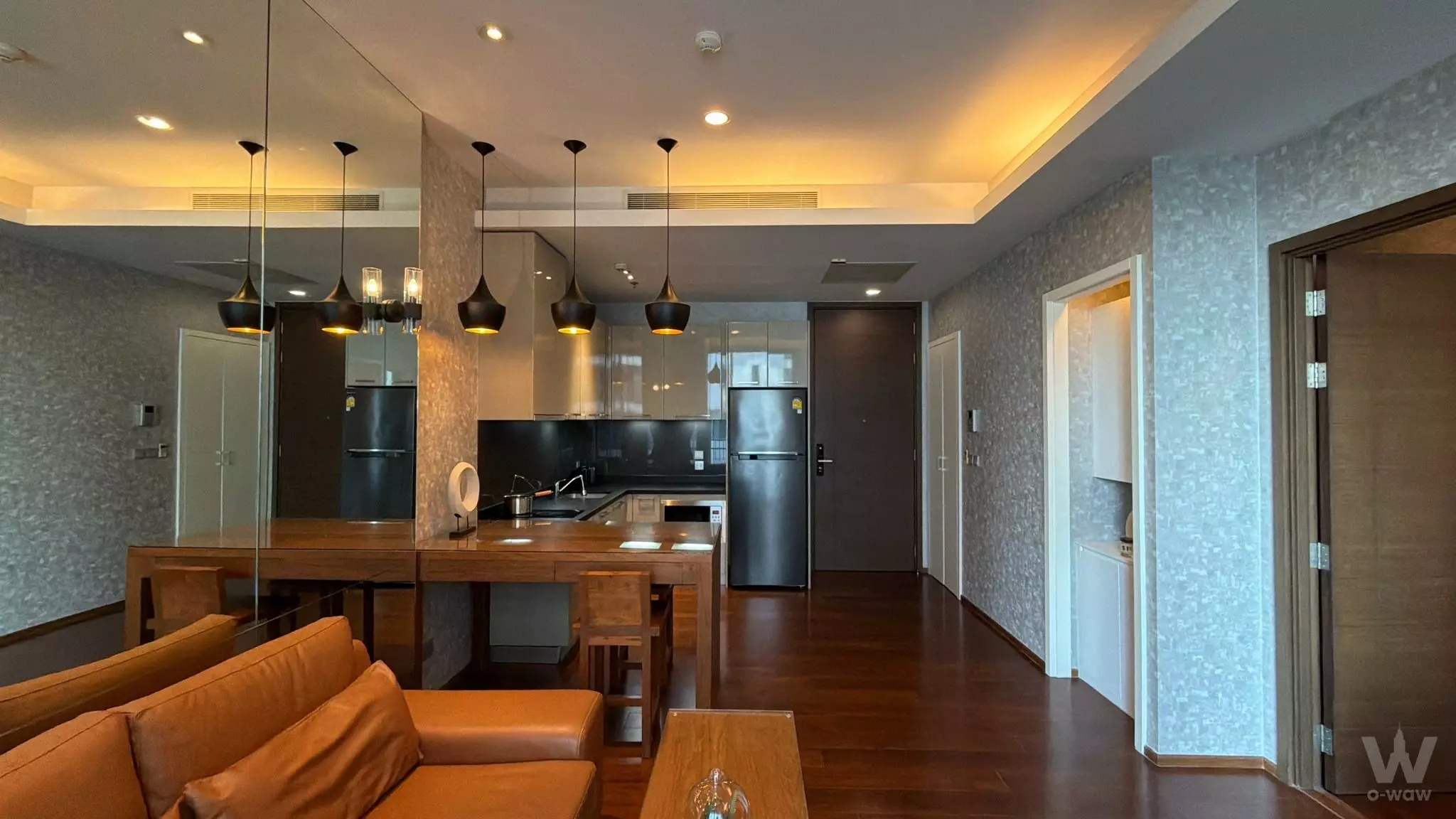 Modern living area with tan leather sofa, dark wood floors, and open kitchen in 1-bed Quattro by Sansiri rental