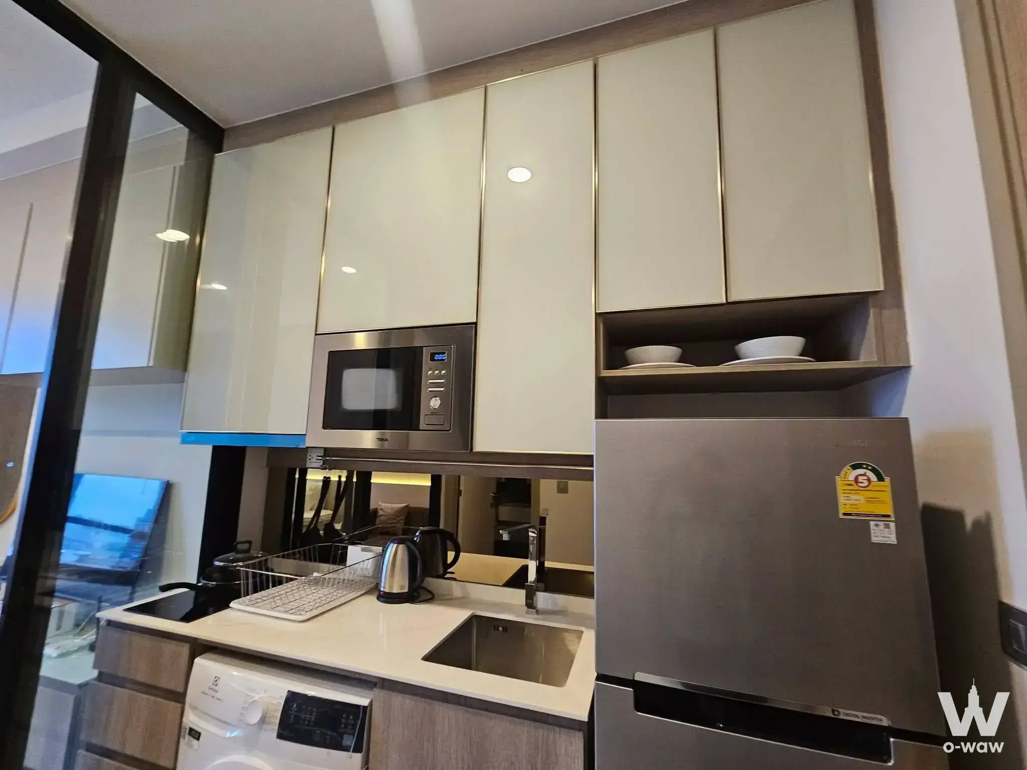Compact kitchenette in a Park Origin Phaya Thai 1-bed condo with cream cabinets, gold trim and stainless appliances