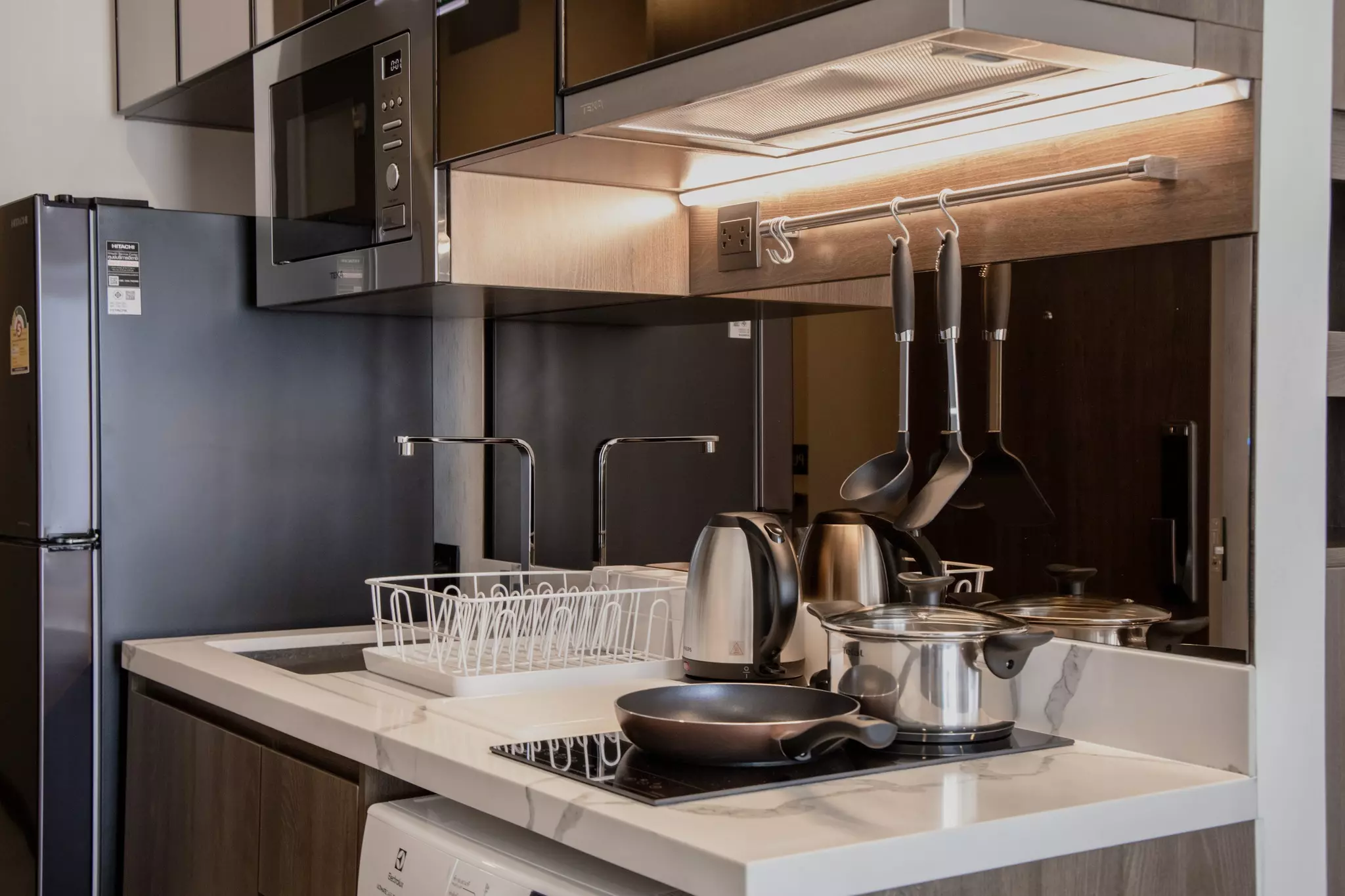 Modern kitchenette with quartz counters, dark cabinetry, and stainless steel appliances in 1-bed condo for rent at Park