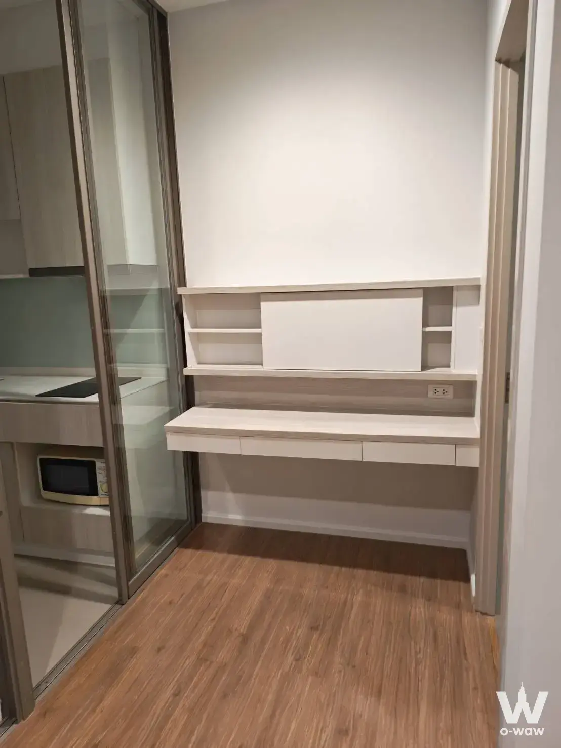 MIT Condo study nook featuring white floating desk, shelving, and glass kitchen partition