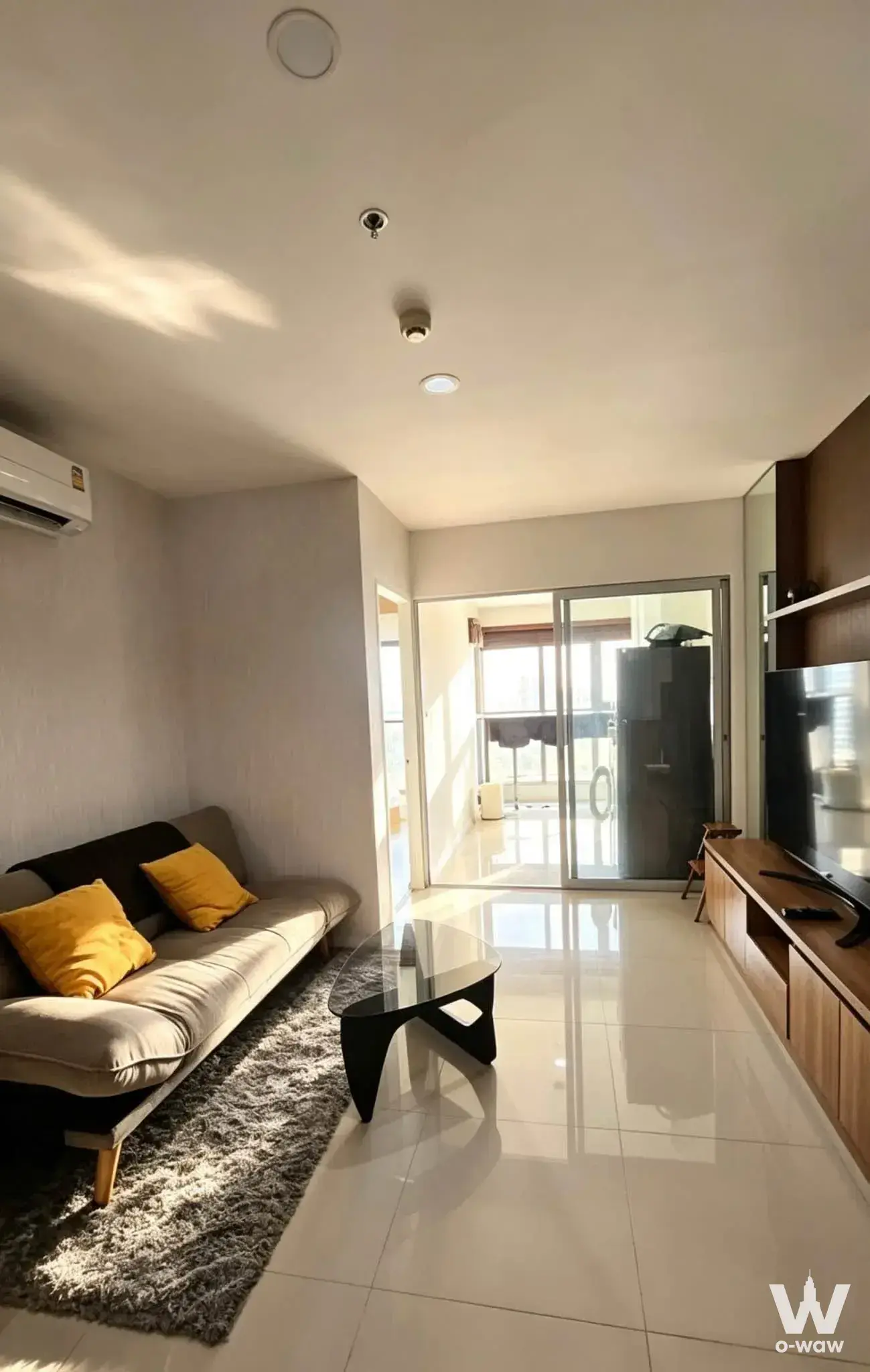 Aspire Sukhumvit 48 living room with grey sofa, yellow pillows, and balcony access