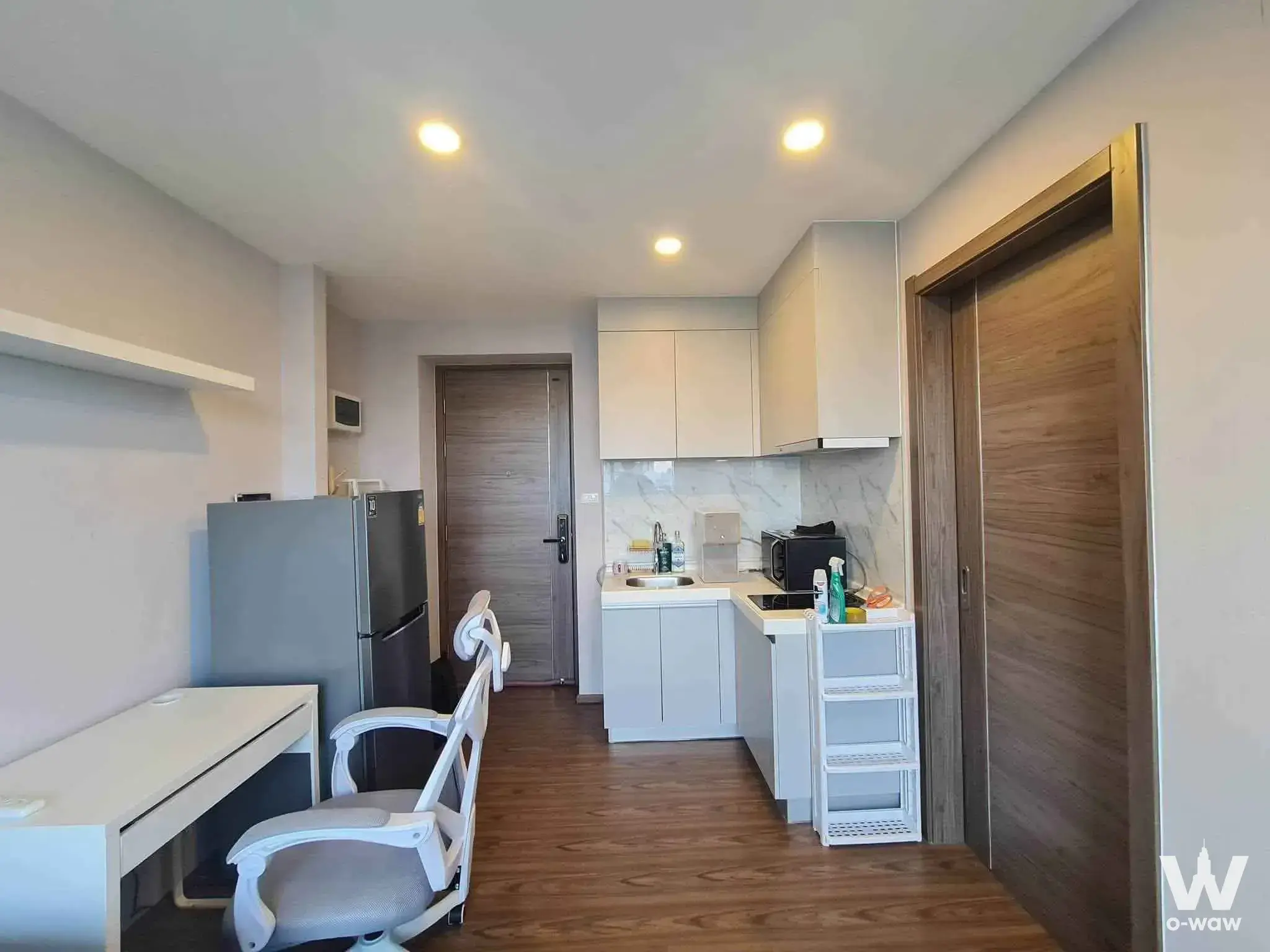 Modern studio interior with wood-laminate floors, white kitchenette, and workspace in Artisan Ratchada 1-bed rental