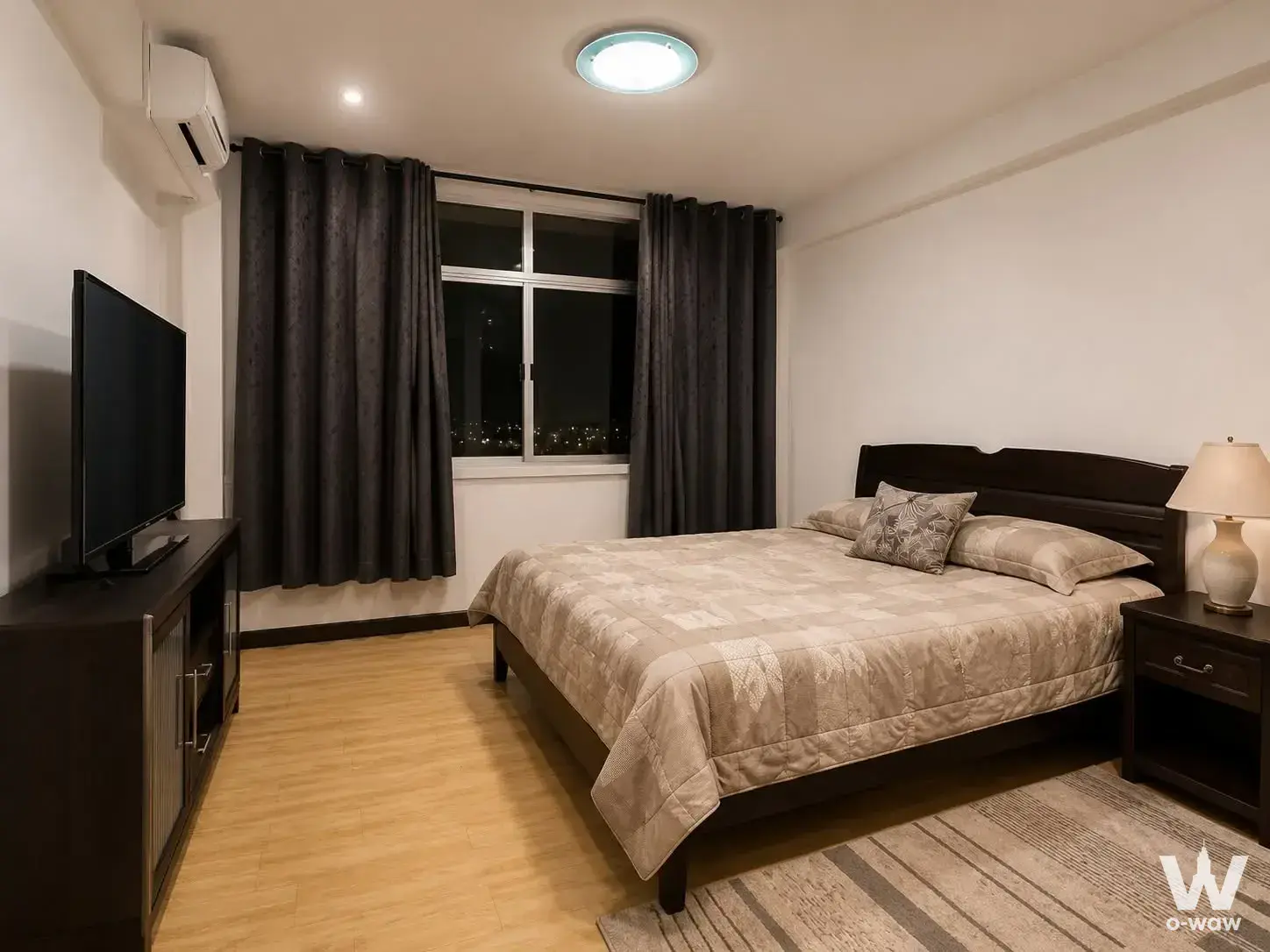 Modern bedroom in 2-bed Siam Condominium with dark wood furniture, city skyline view, and light wood flooring