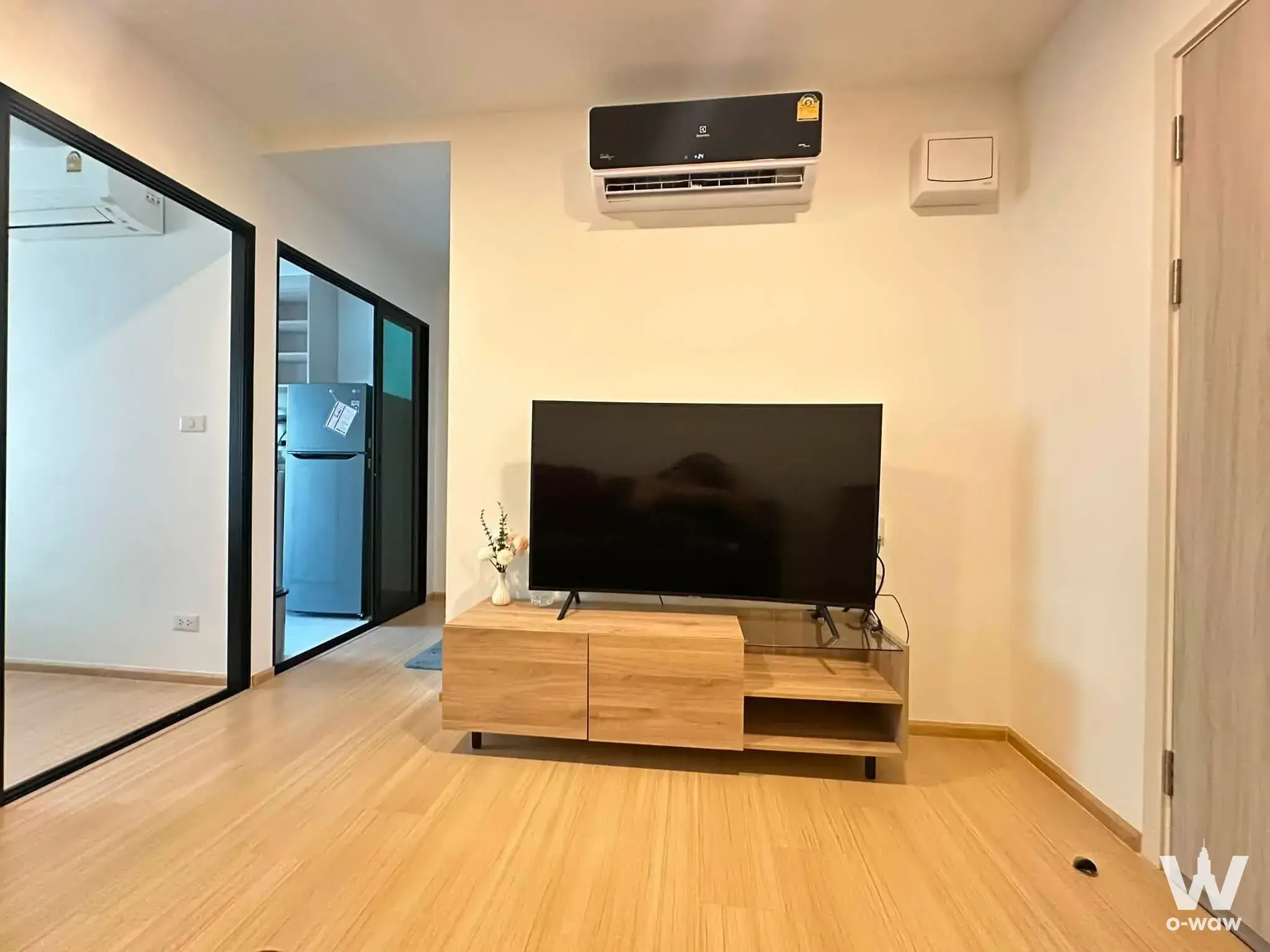 Modern living room with oak media console, TV, and sliding doors in Chewathai Hallmark Ladprao condo for rent