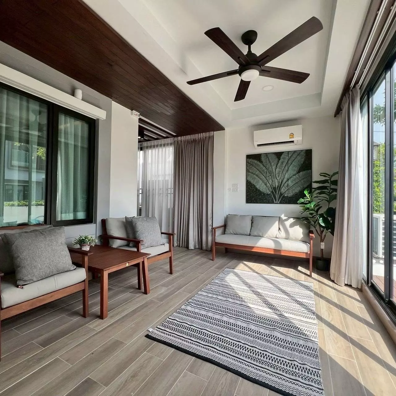 Semi-outdoor balcony with dark wood seating, geometric rug, and glass doors at 4-bed house for rent in Areeya Como Primo