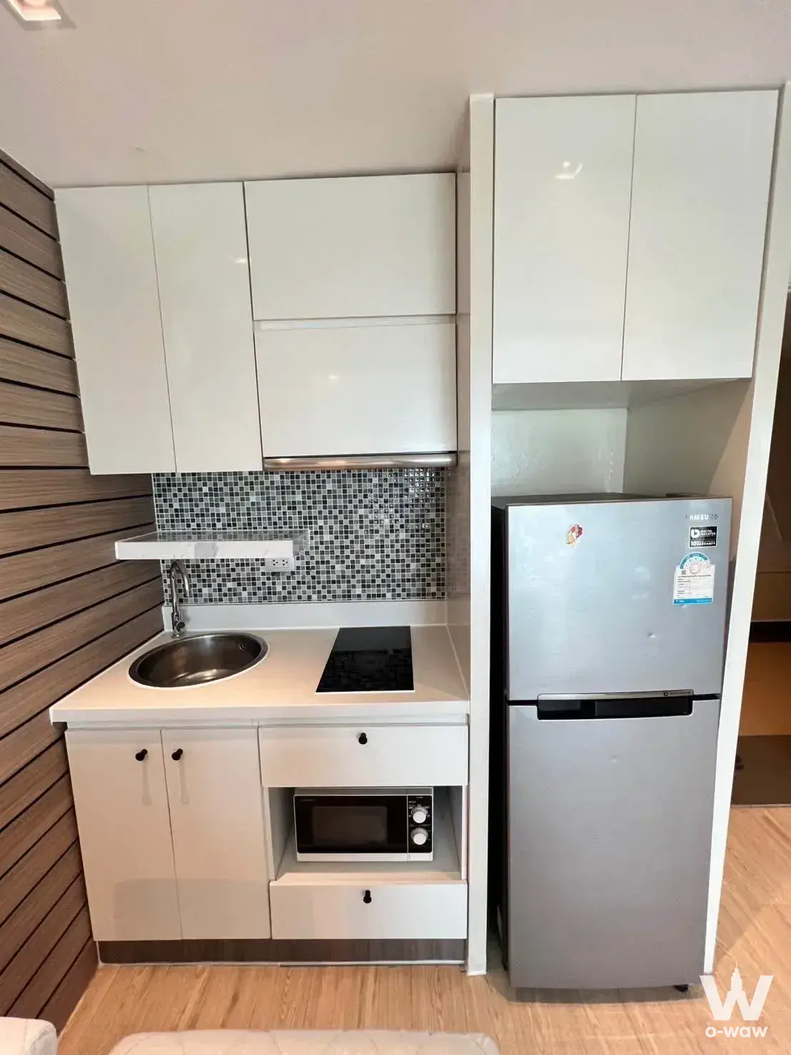 Compact La Santir condo kitchenette with glossy white cabinets, induction cooktop, and wood-slat accent wall