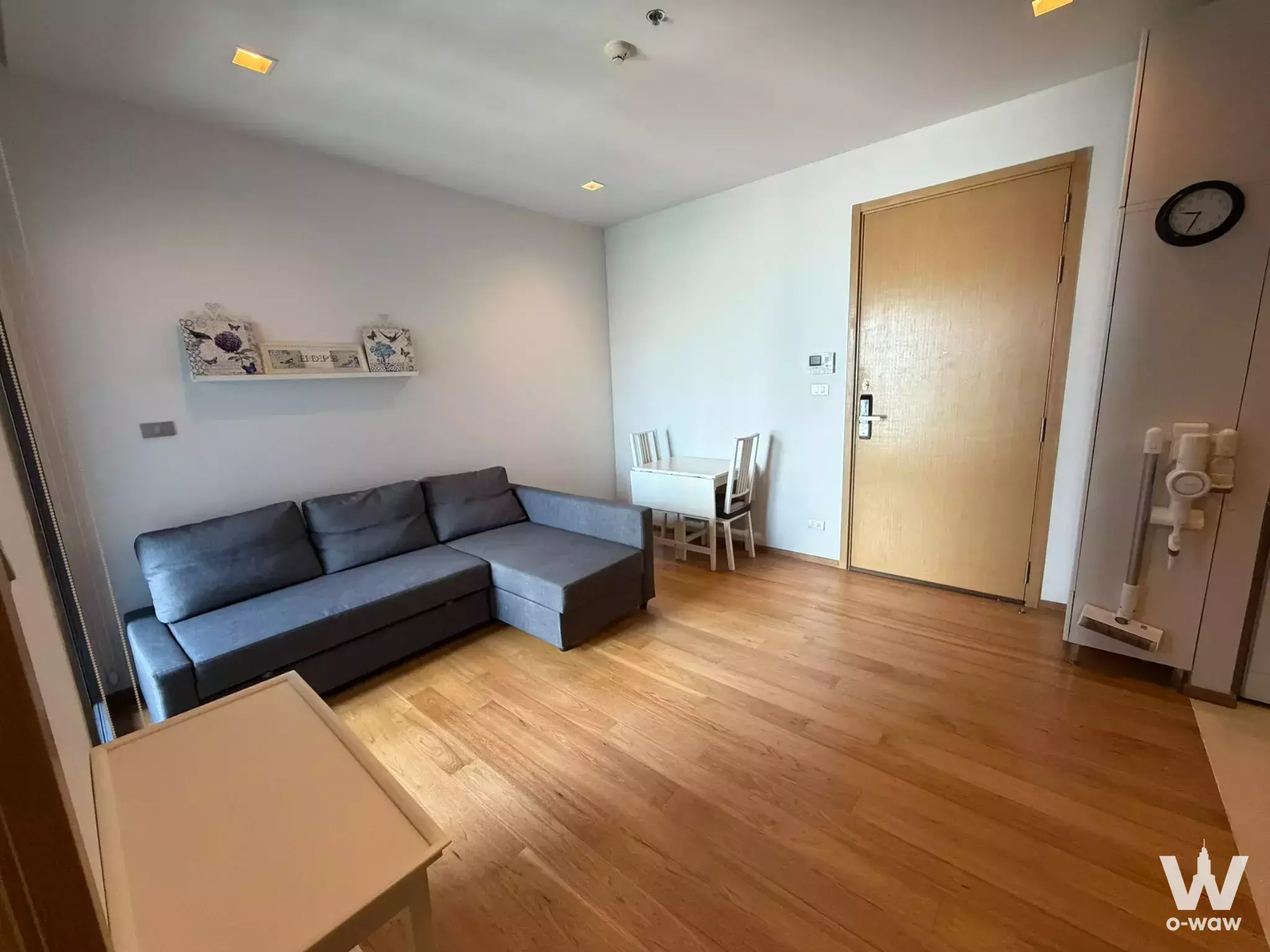 Bright open-plan living and dining area in Hyde Sukhumvit 13 condo with oak floors, grey sofa, and white table