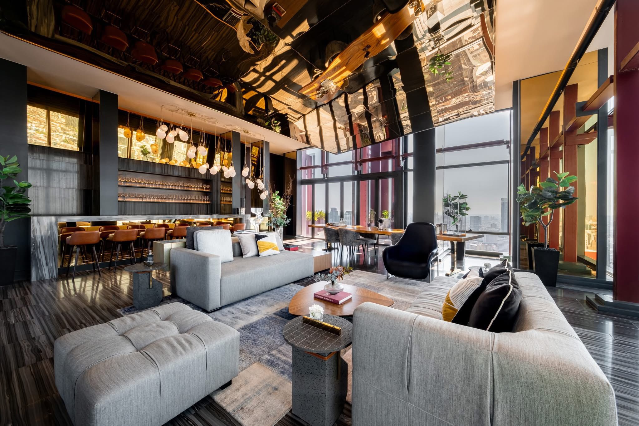 Modern lounge at Ashton Silom condo with mirrored ceiling, bar stools, and panoramic city skyline views through
