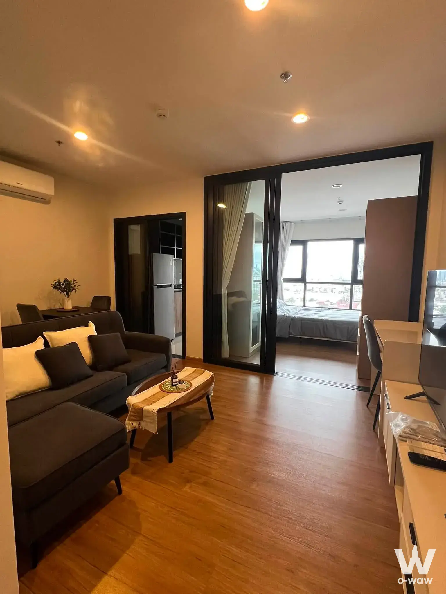 Furnished living room in The Line Vibe 1-bed condo with brown sectional sofa and open view to bedroom