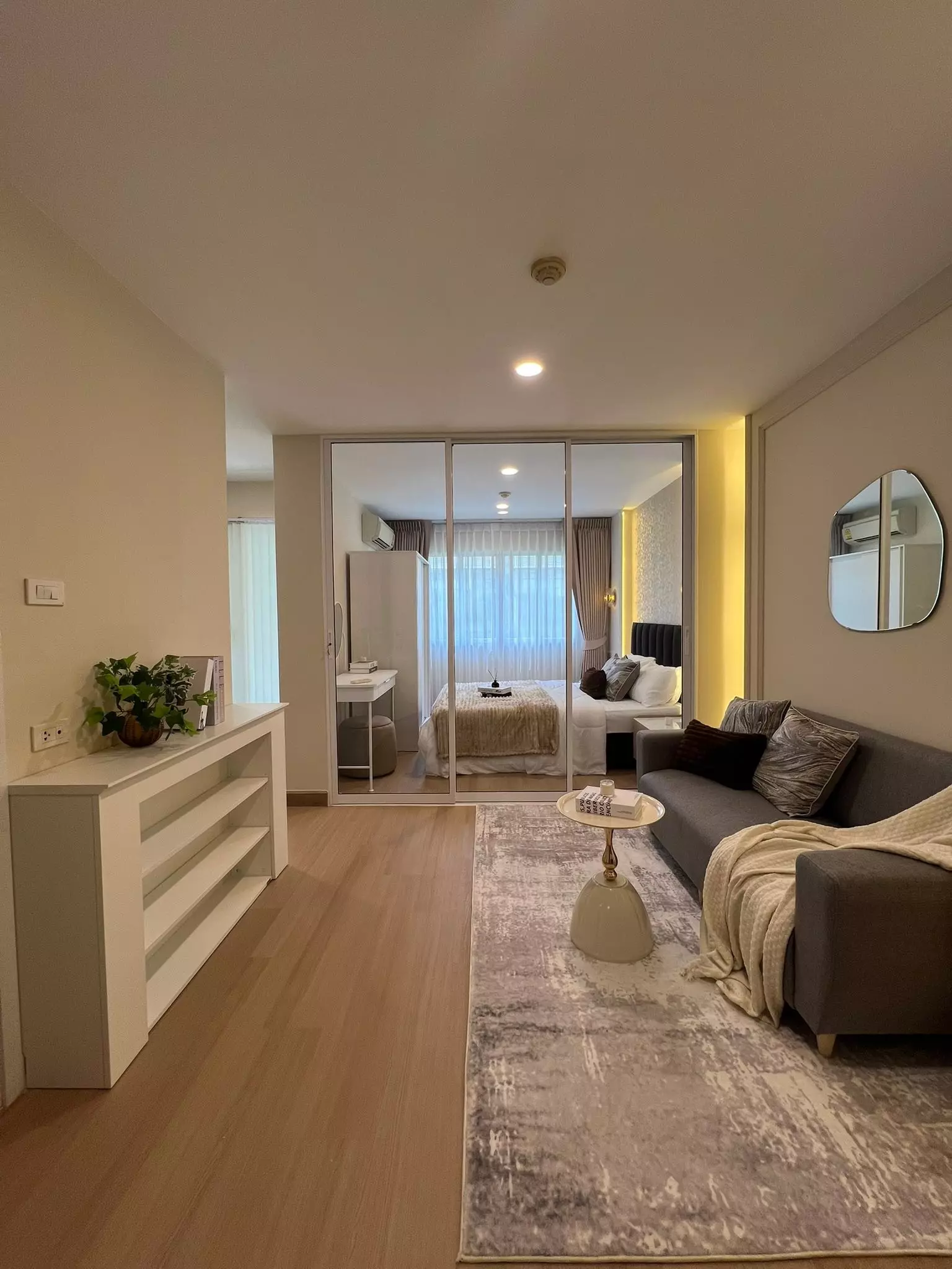 Modern 1-bed condo in Lumpini Town Bodindecha with open-plan living, sliding glass doors, gray sofa, and wood flooring