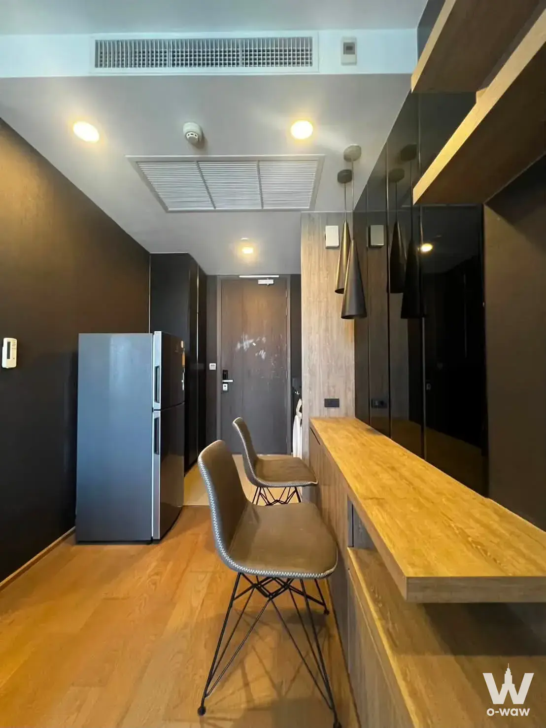 Compact kitchenette in the Ashton Chula-Silom rental has a floating oak counter with bar stools and dark charcoal walls