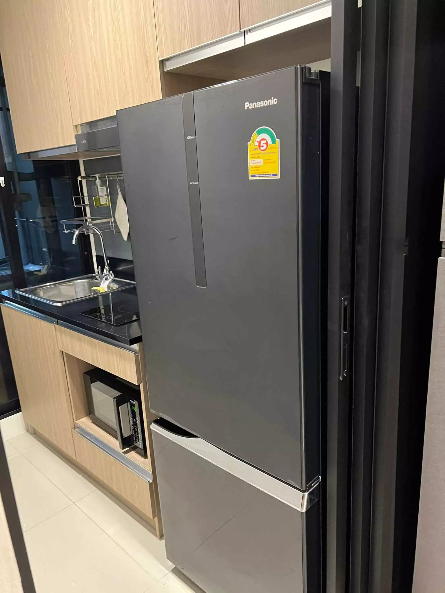 Modern kitchenette with light wood cabinets, black countertops, and stainless steel sink in 1-bed condo for rent at Niche