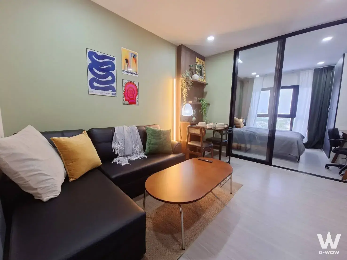 This Sukhumvit City Resort 1-bed condo for rent has a living room with a black leather sectional and a glass partition