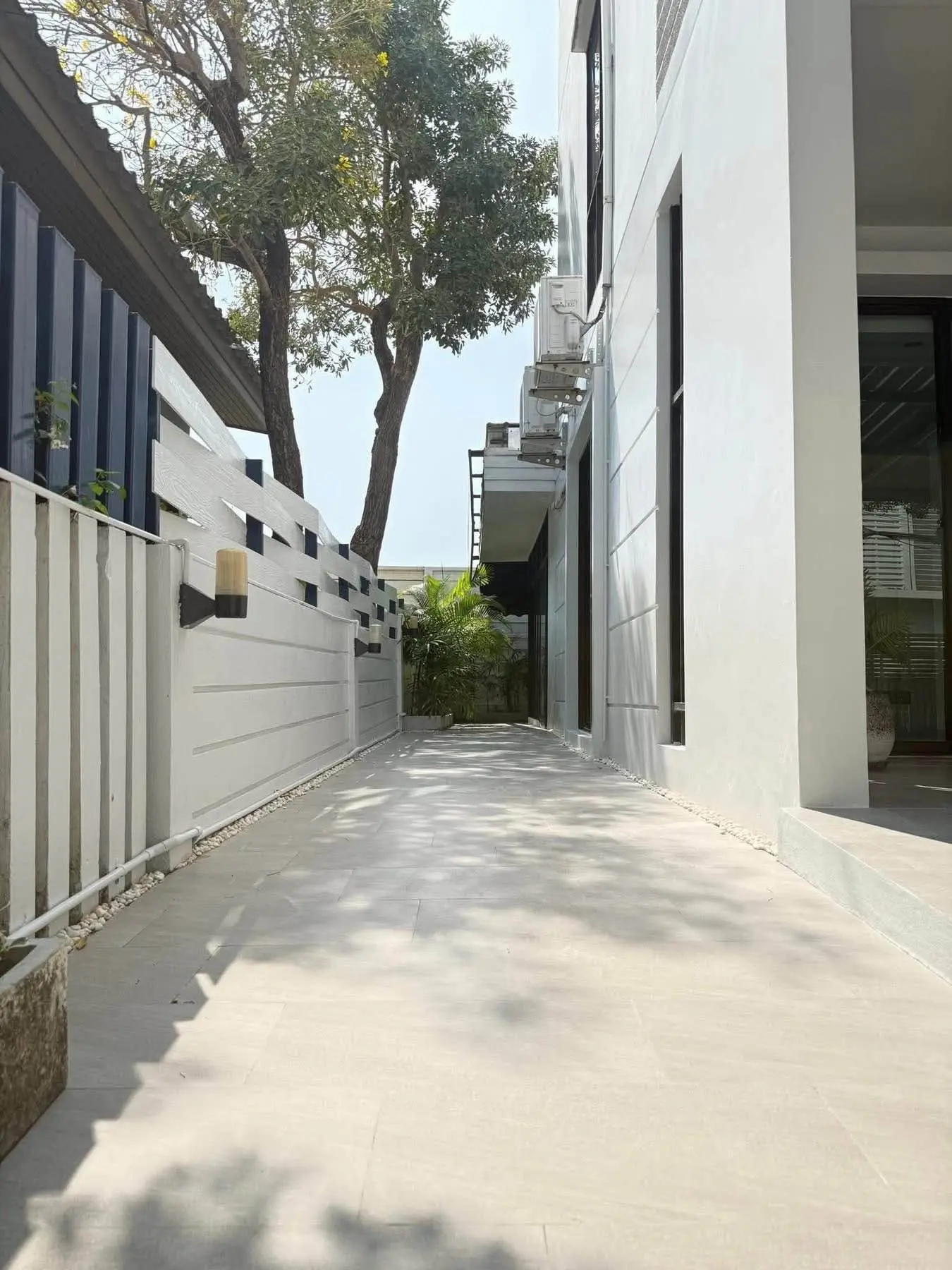 Narrow tiled side yard with navy slat fence and white building facade at Areeya Mandarina Sukhumvit 77 townhouse