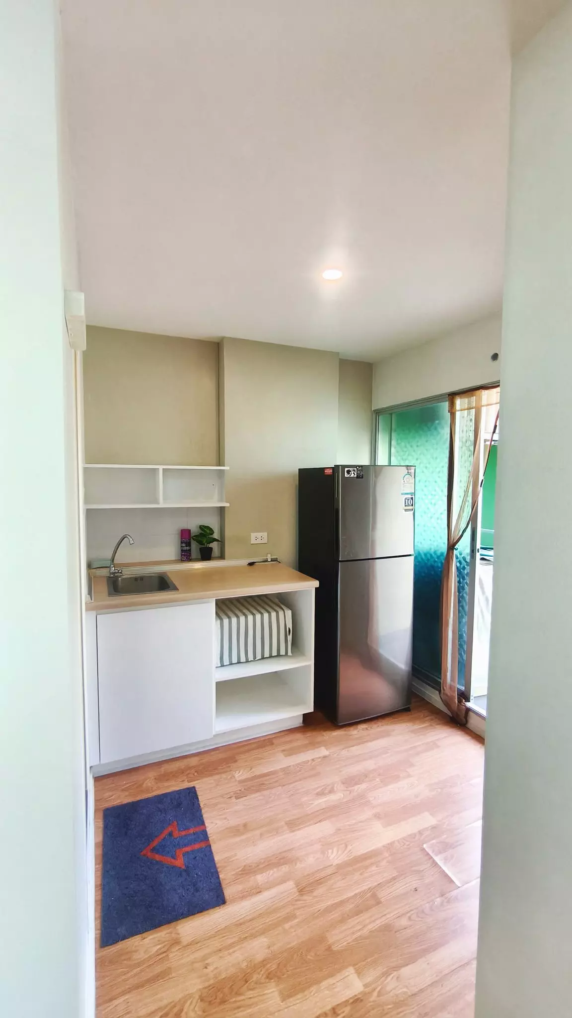 Compact kitchenette with white cabinetry, stainless steel fridge, and sliding glass door to balcony in Lumpini Ville