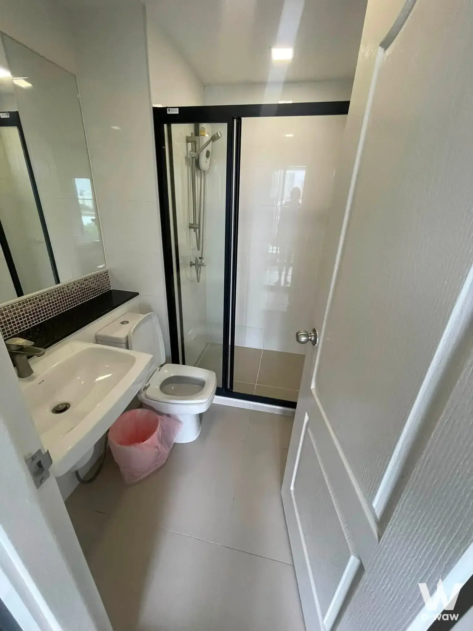 Compact modern bathroom featuring black granite countertop, mosaic backsplash, and frameless mirror at The 1 Plus Grand