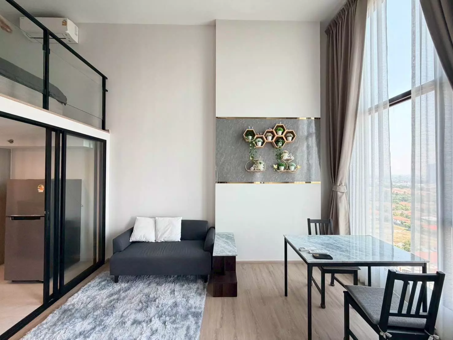 Modern 1-bed condo interior with mezzanine loft, grey sofa, marble dining set, and city views at Origin Plug & Play