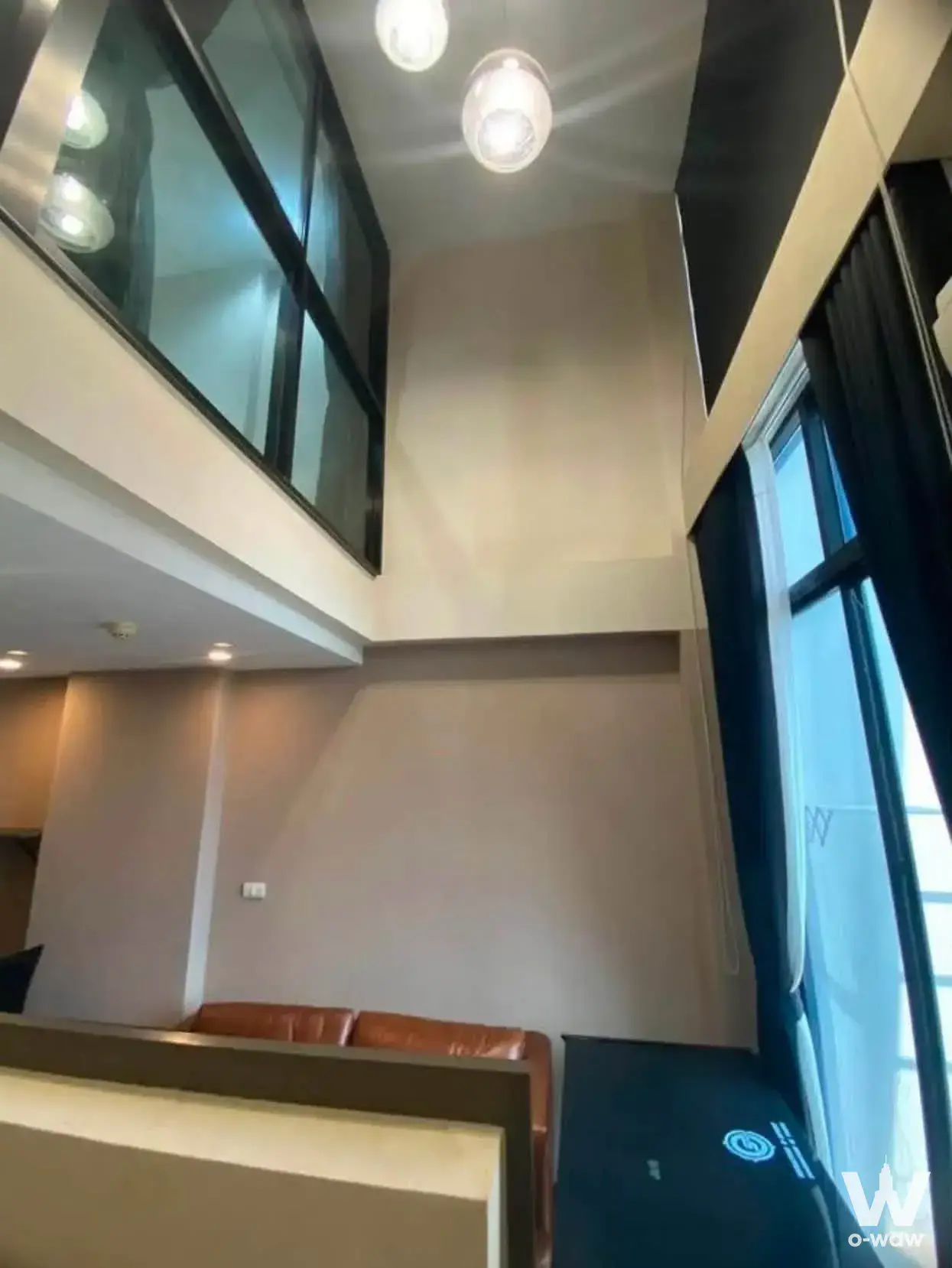 Duplex living room with high ceilings, glass mezzanine railing, and pendant lights in 1-bed condo for rent at Beyond