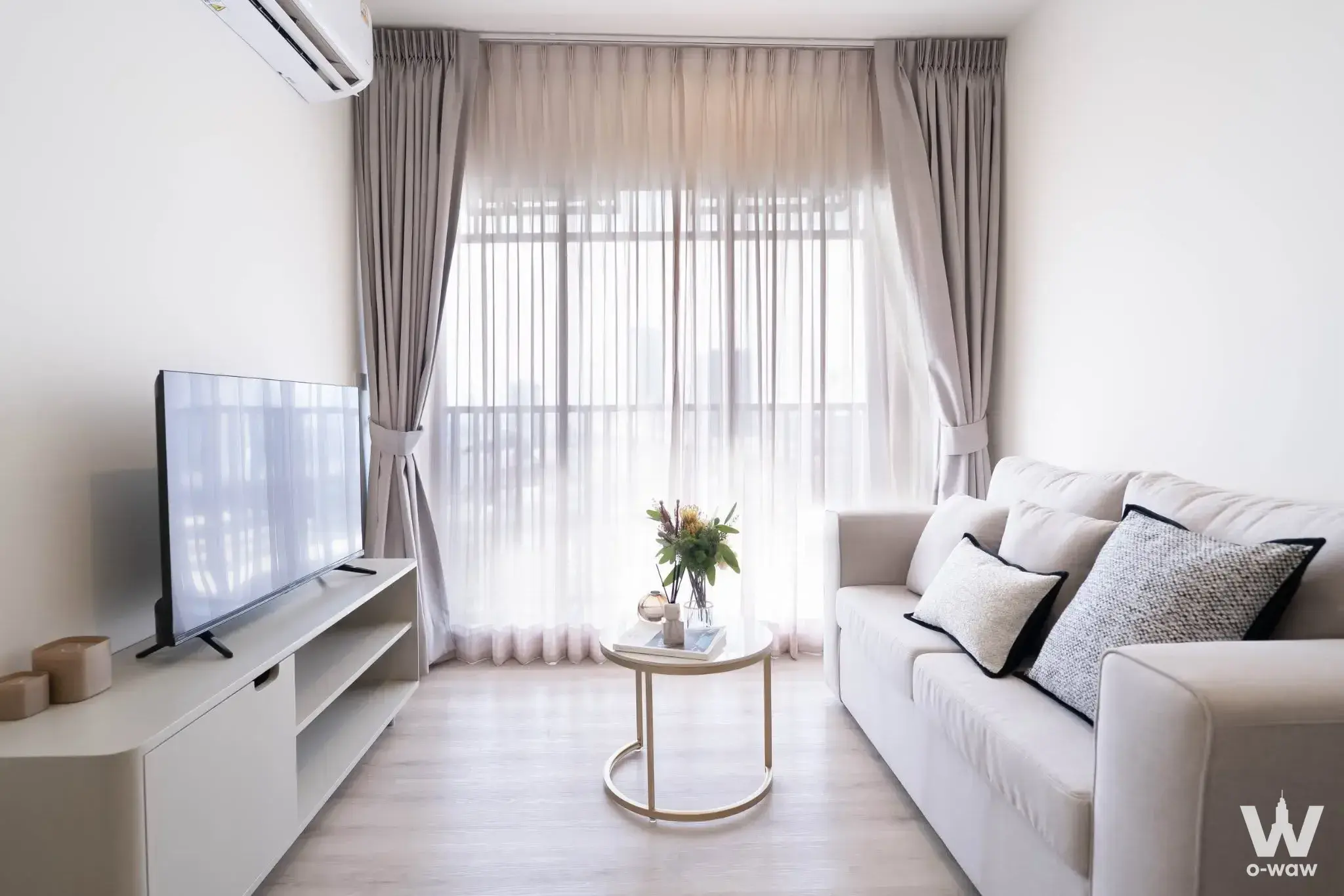 Bright living room in this Origin Place Bangna condo features a grey sofa and floor-to-ceiling windows with sheer curtains