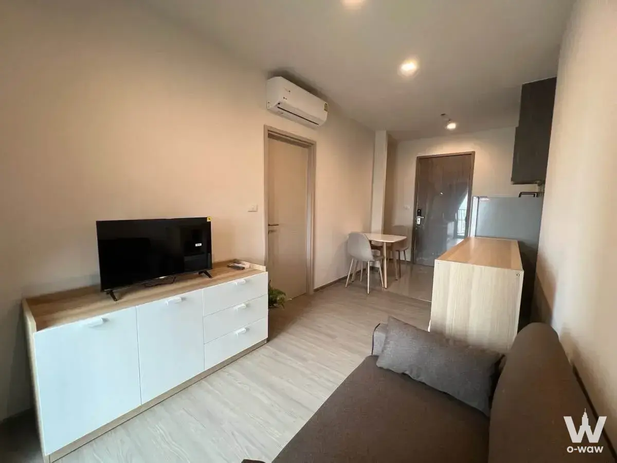 Modern 1-bed condo living room in THE BASE Phetchaburi-Thonglor with beige sofa, TV unit, and open kitchenette