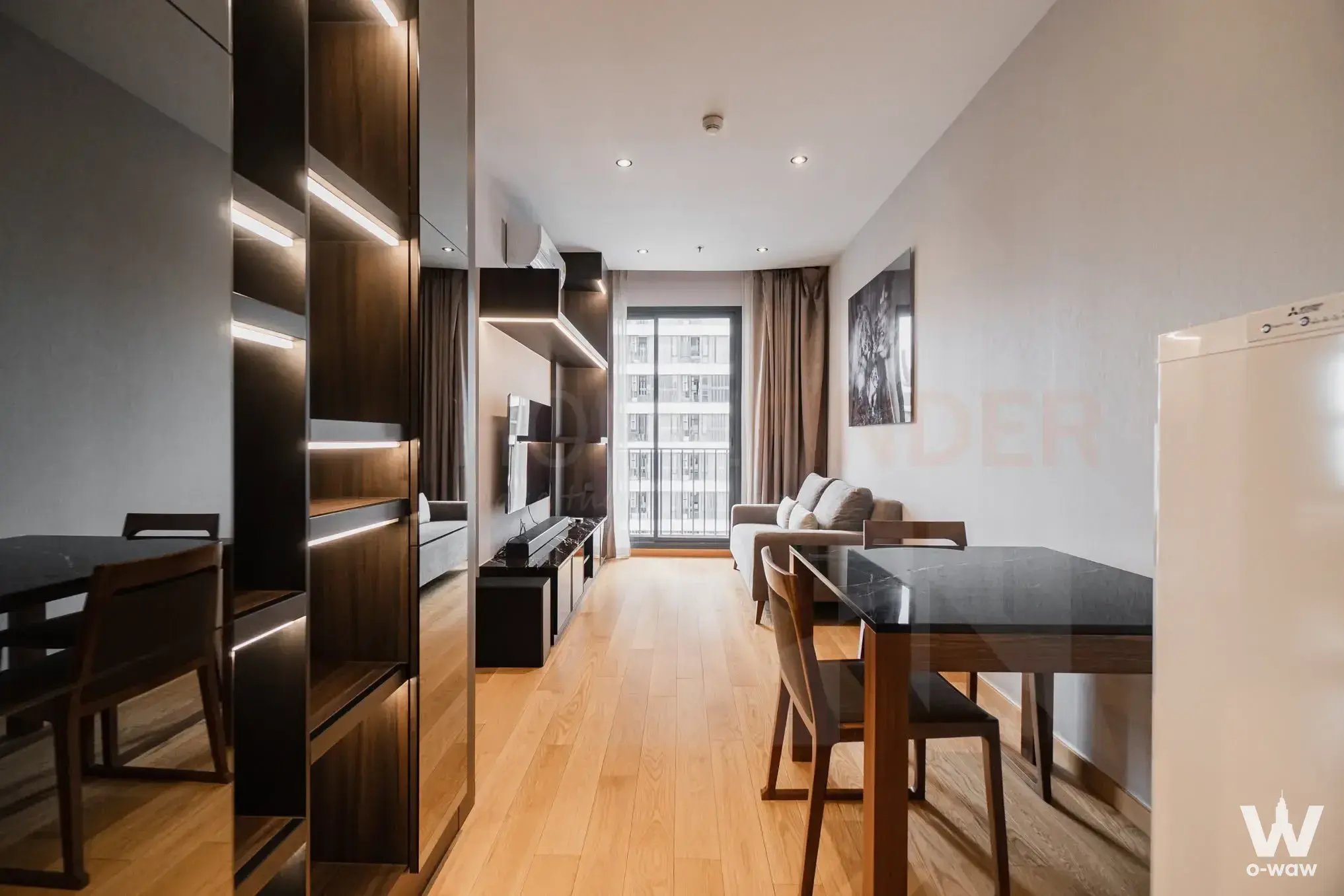 Modern living and dining area in M Thonglor 10 condo with oak floors, grey sofa, and balcony access