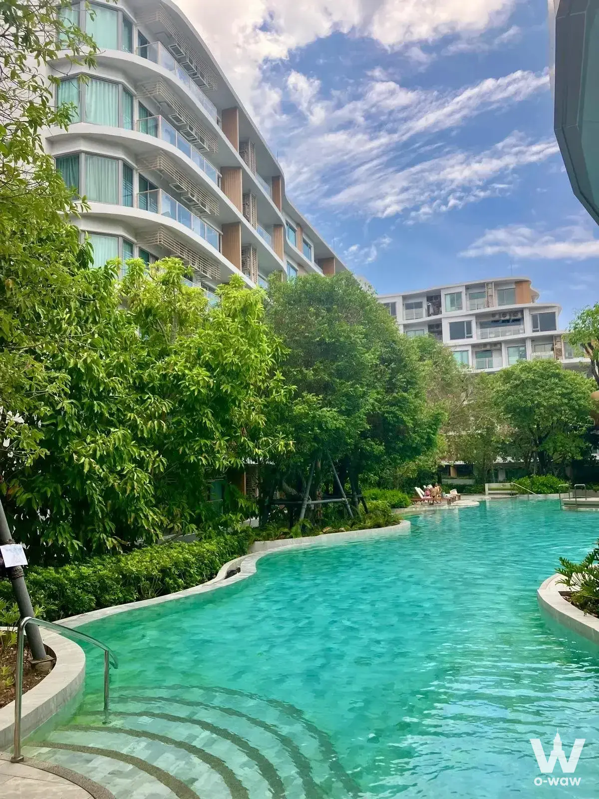Turquoise curved pool with stone coping and lush greenery at a 1-bed condo for sale in Phyll Phuket