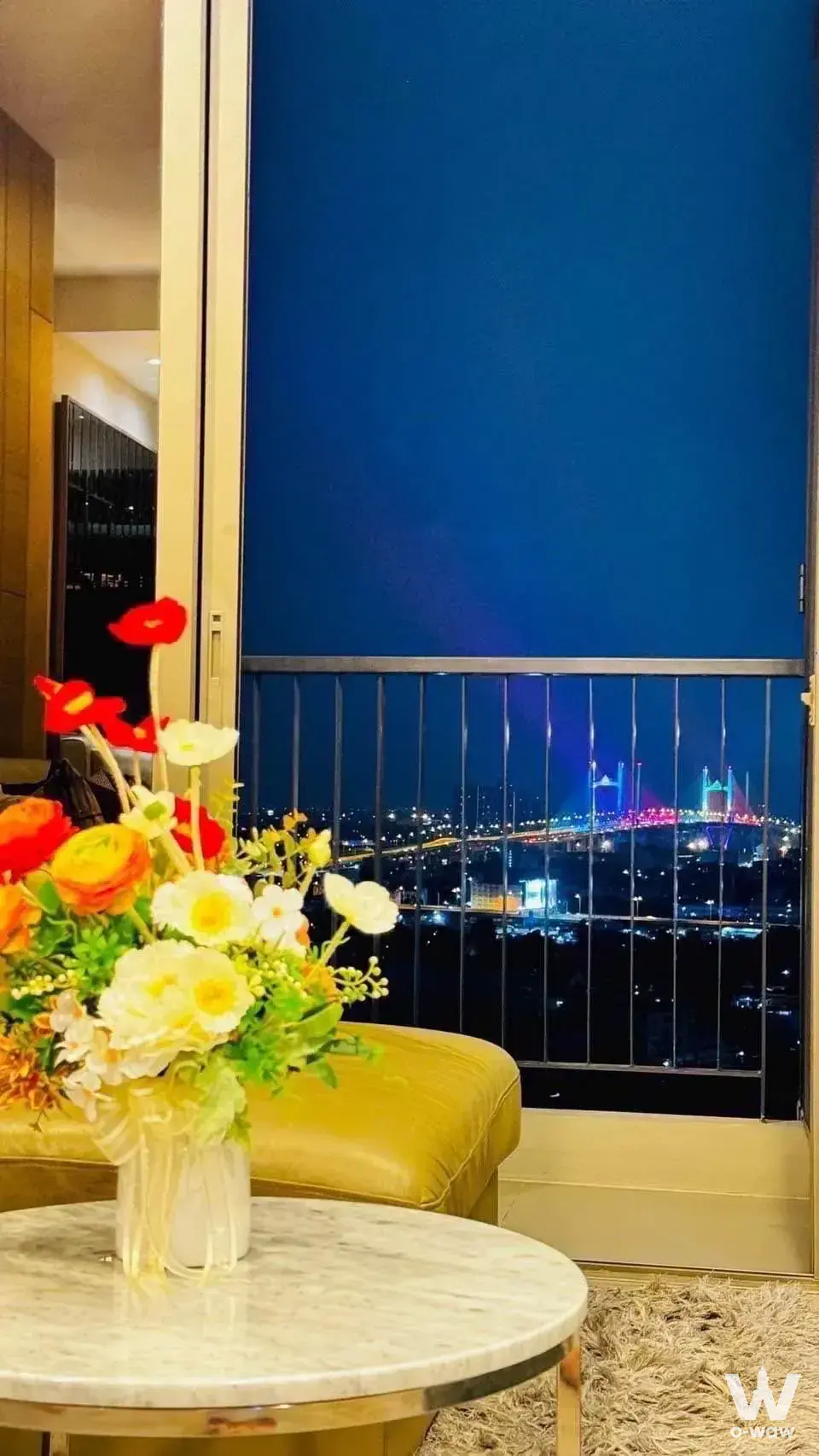 Living room with marble coffee table and balcony view of illuminated suspension bridge in 2-bed condo for sale at The Room