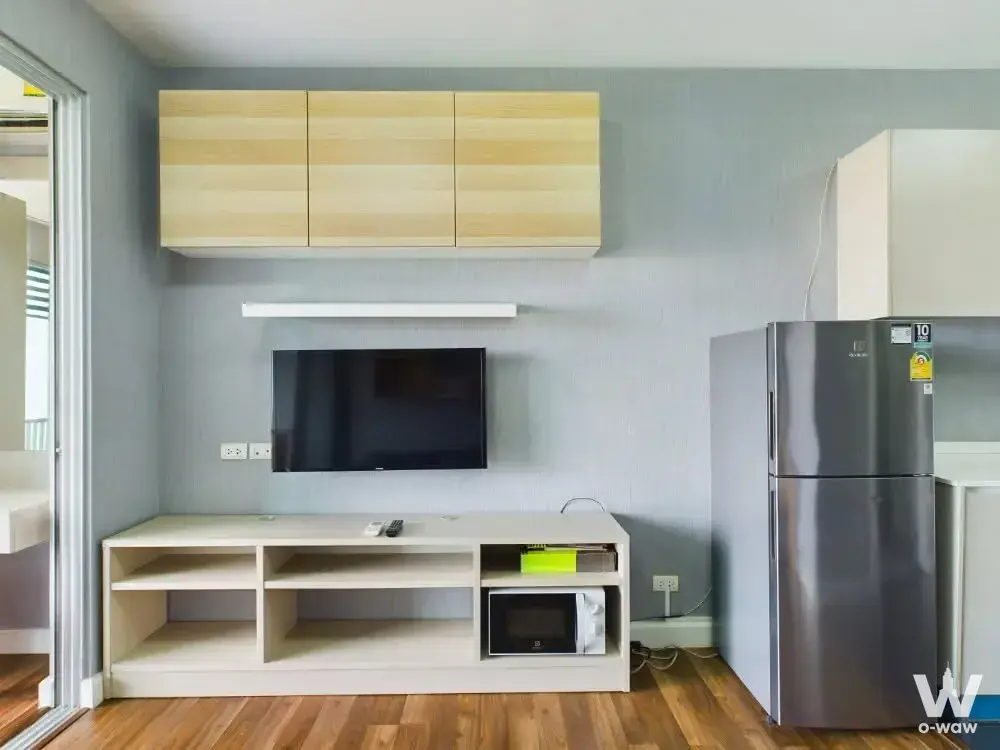 Bright studio living area with wall-mounted TV, white media console, and stainless steel fridge in A Space ME Sukhumvit 77