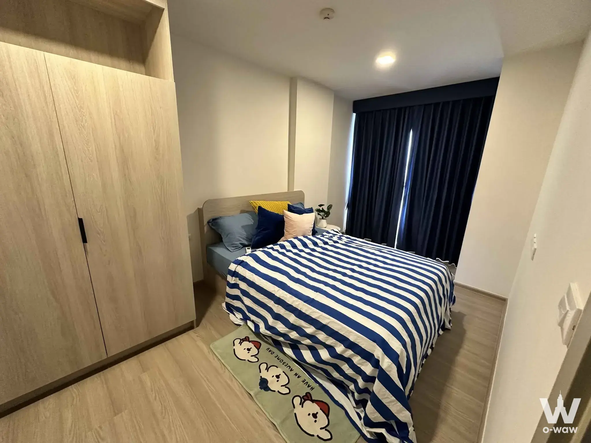 Furnished bedroom in a Dcondo Reef Phuket 2-bed condo with striped duvet, oak wardrobe, and navy curtains