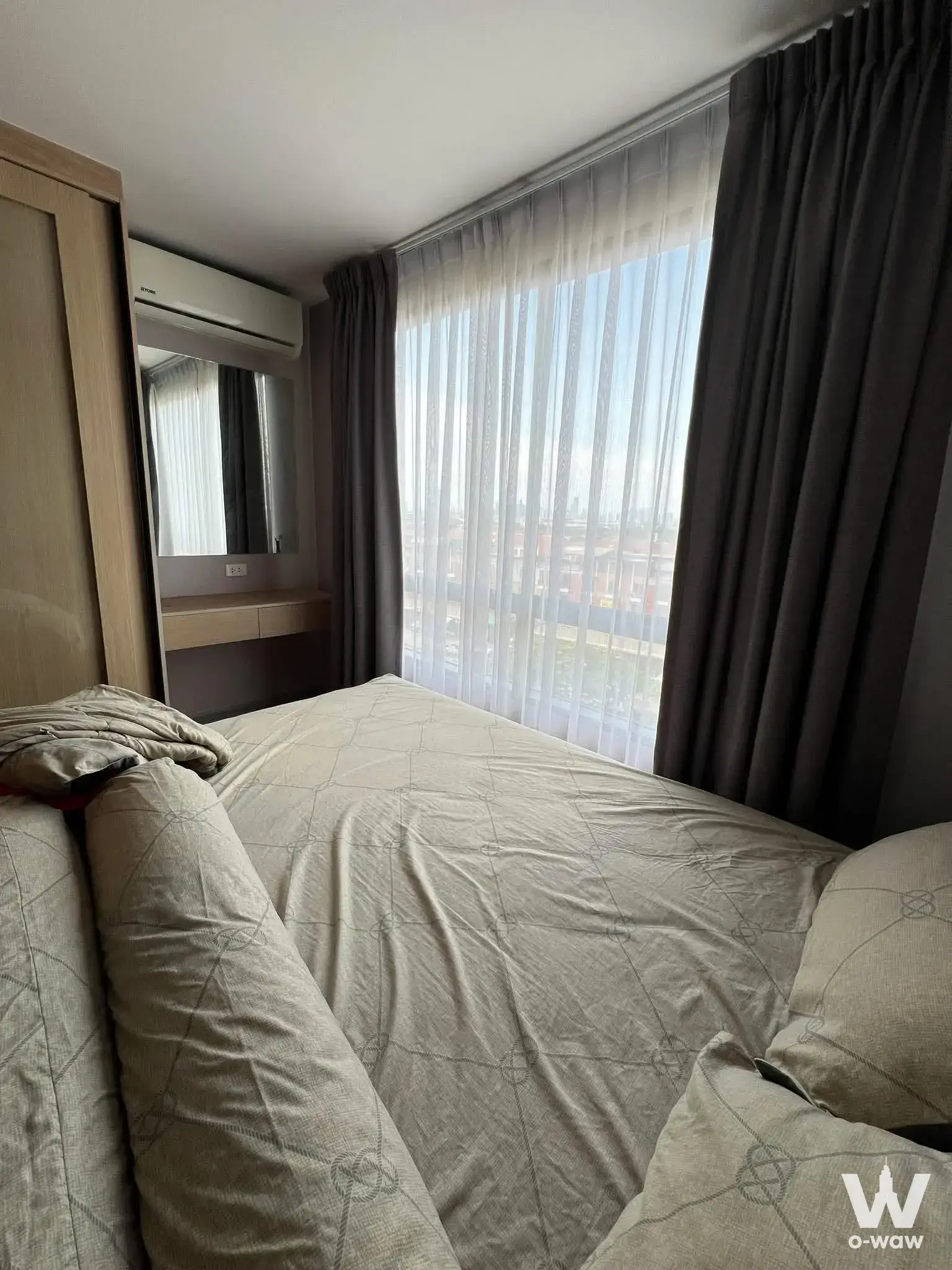 Queen bed with beige linens in 1-bed Polis Condo bedroom featuring oak wardrobe and large window with grey drapes