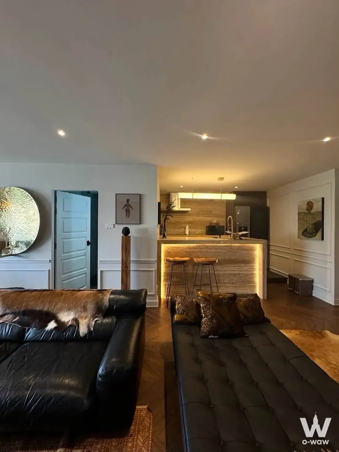 Open-plan living room and kitchen in a Sukhumvit 26 condo featuring black leather seating and dark herringbone floors