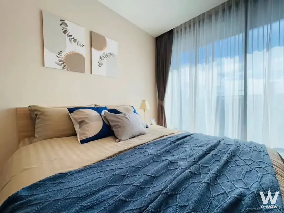 Modern bedroom in 1-bed condo for rent at XT Phayathai featuring floor-to-ceiling windows and blue-accented bedding