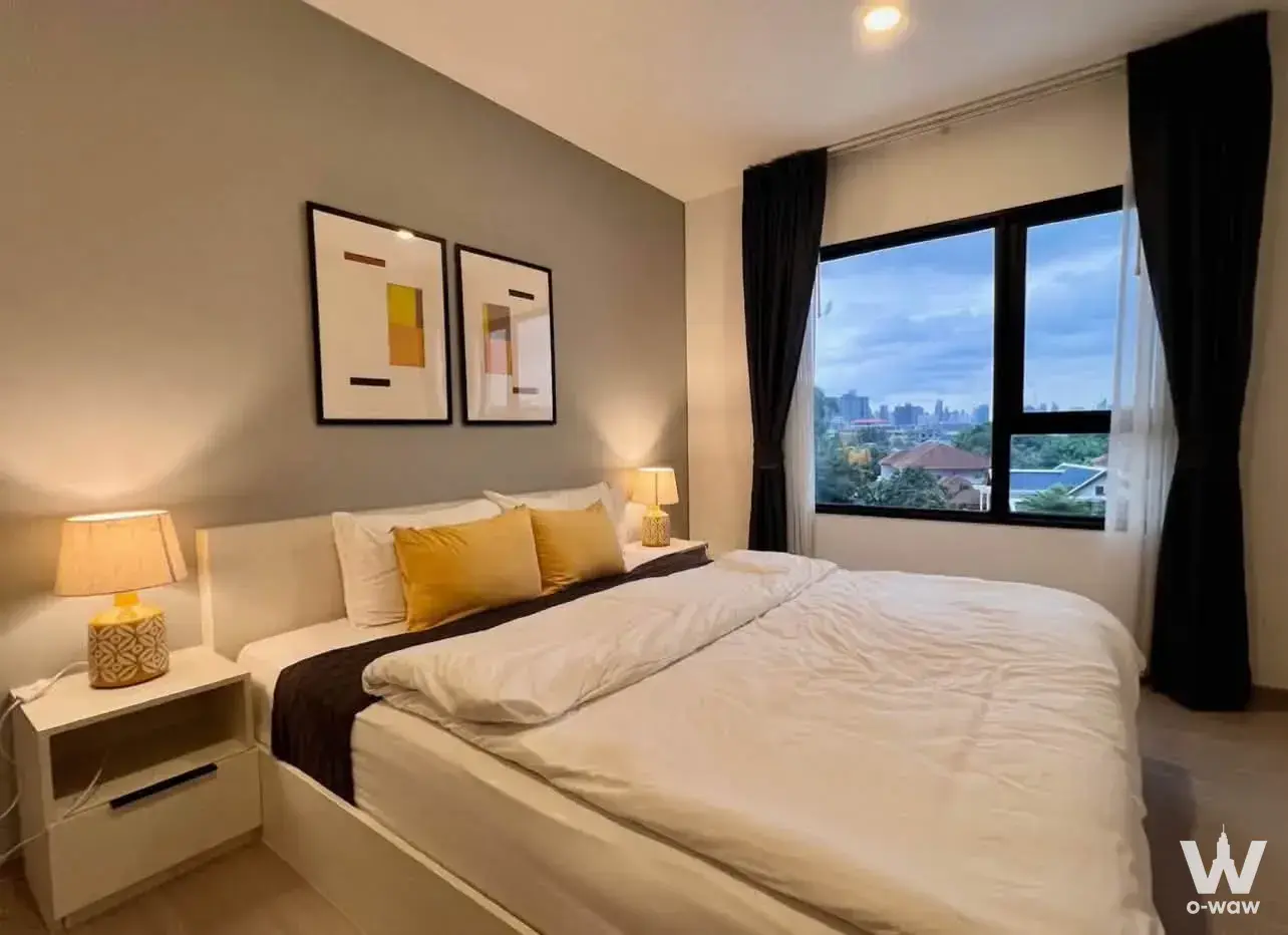 Queen bed with mustard pillows in a furnished bedroom at Aspire Sukhumvit-On Nut
