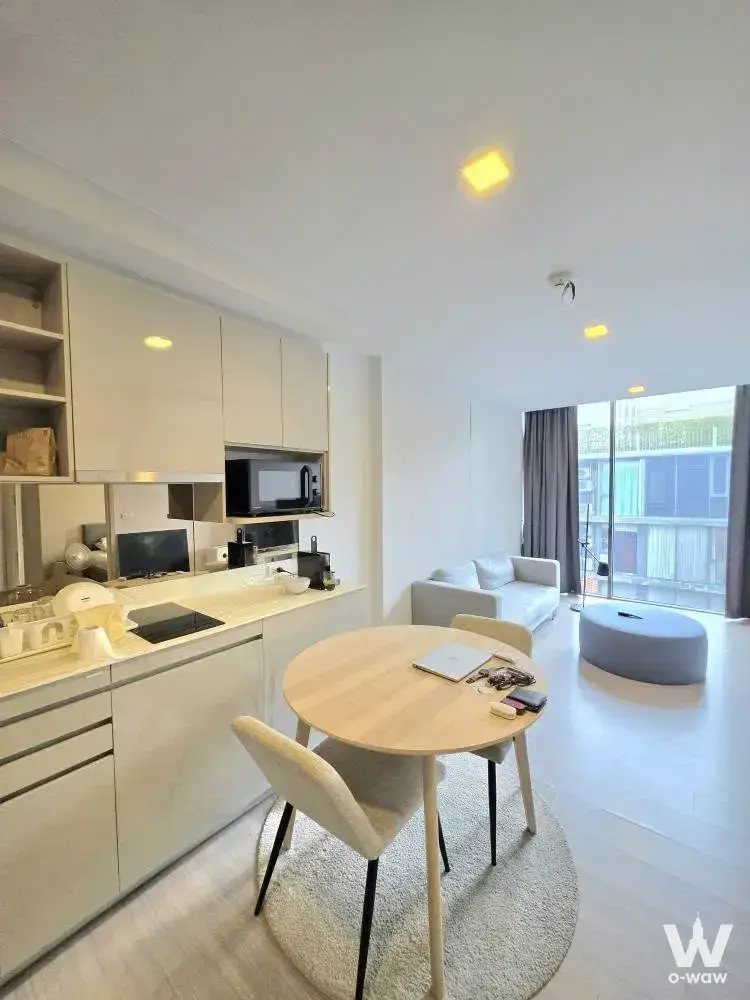 Modern studio condo with integrated kitchenette, round dining table, and balcony access in Bangkok