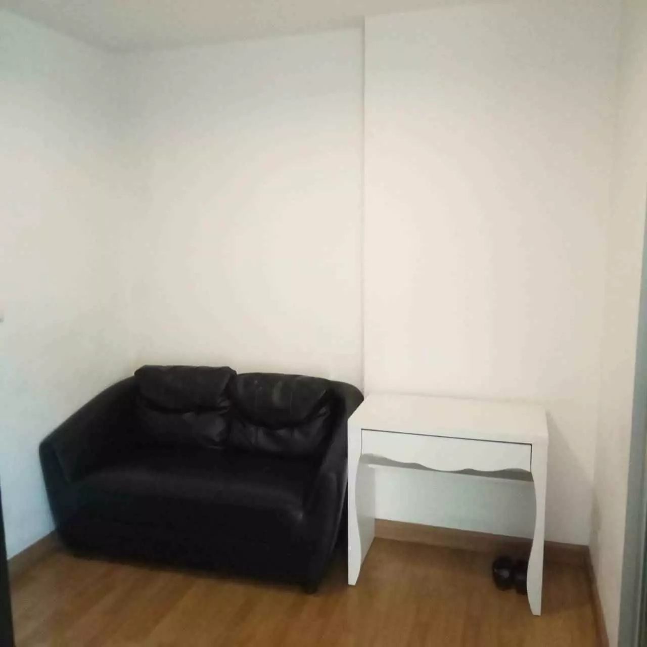 Black leather sofa and white desk in minimalist living area of 1-bed condo for rent in Aspire Rama 4