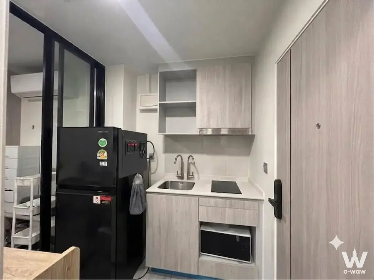 Compact kitchenette in a 1-bed Atmoz Tropicana Bangna rental with light wood cabinets and black induction cooktop